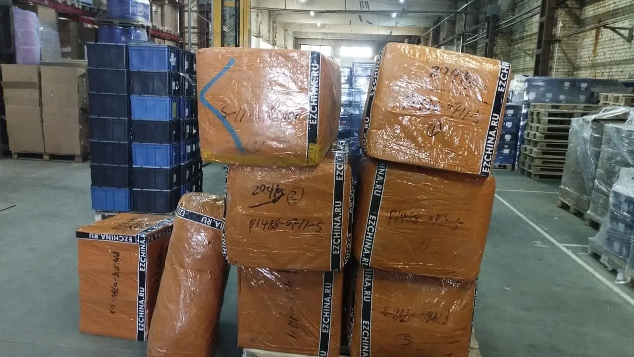Коробки и мешок в оранжевой плёнке с лентой EZCHINA.RU, сложенные на складе