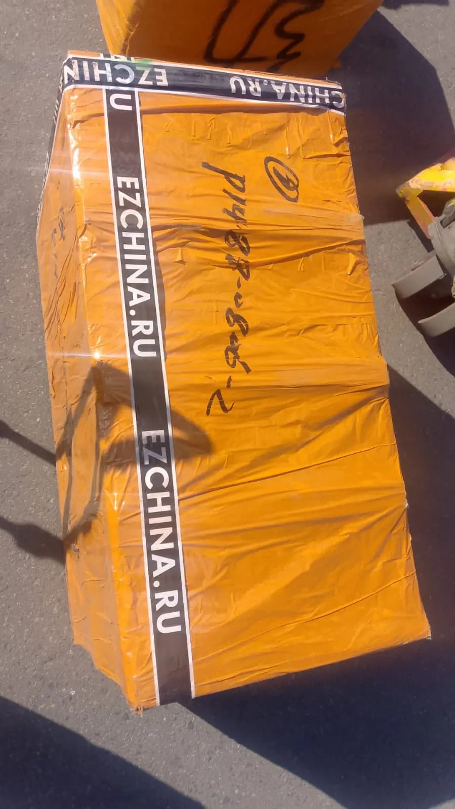 Коробка в оранжевой плёнке с лентой EZCHINA.RU на площадке у склада